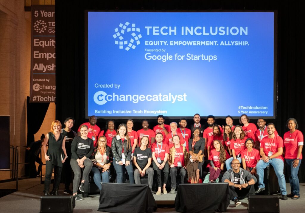 A group of several Tech Inclusion workers in a group photo on stage wearing matching red t-shirts