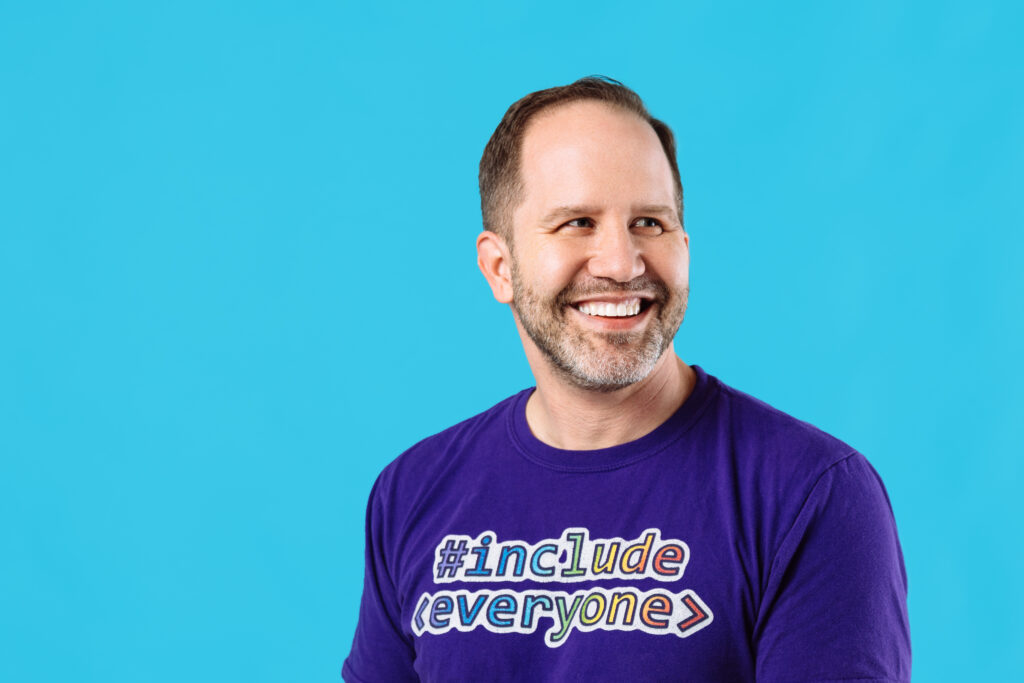 Headshot of Scott Hanselman, who has a salt and pepper beard and brown hair and is wearing a purple shirt that says "include everyone."
