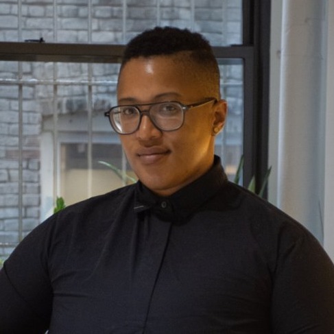 Headshot of Sloan Leo, a Black a non-binary queer person wearing a black shirt and glasses, black hair