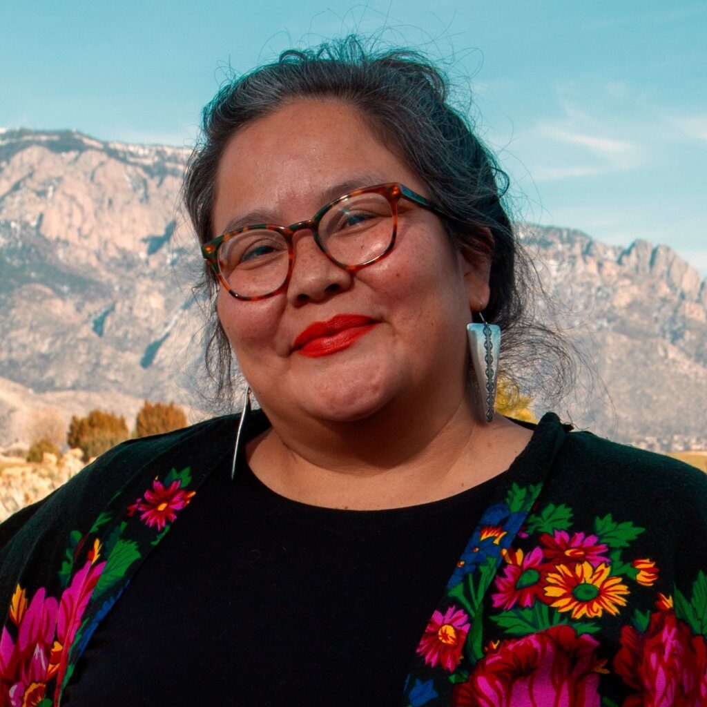 Headshot of Vanessa Roanhorse, a Diné woman with hair pulled back, glasses, and a floral top