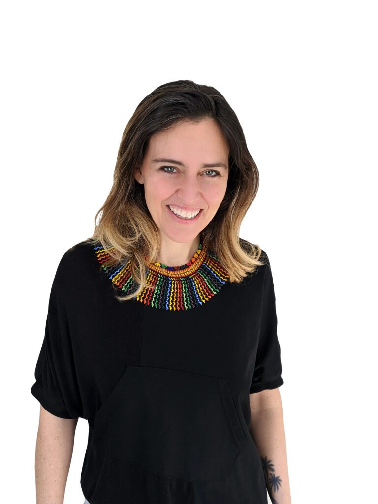 Headshot of Valentina Jaramillo, a LatinX, gender non-conforming person with long dark blonde hair and a black shirt with a multi-colored collar, smiling at the camera.