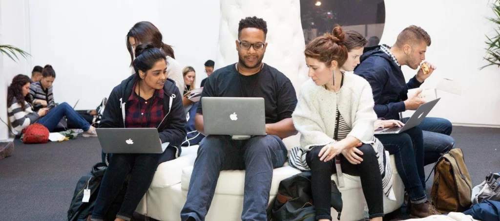 diverse people sitting around a circular couch with laptops communicating with each other