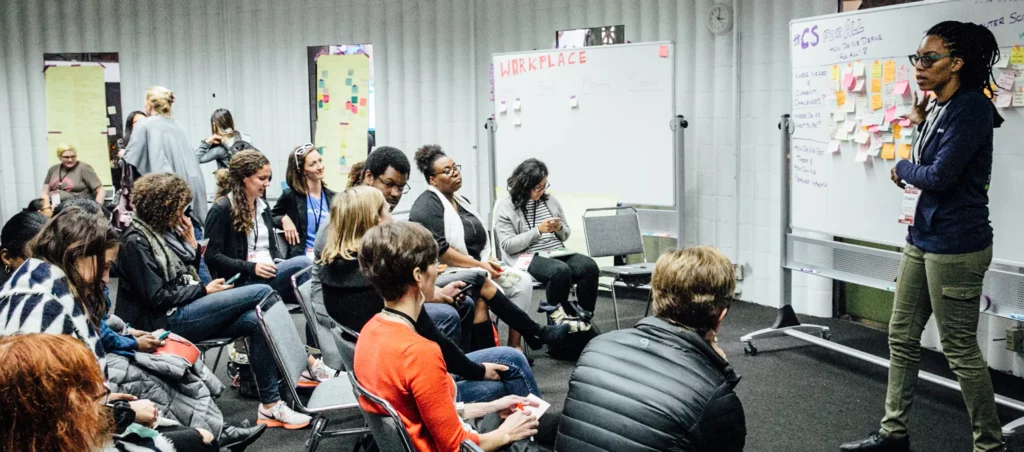 diverse people sitting in chairs facing a whiteboard with someone presenting them