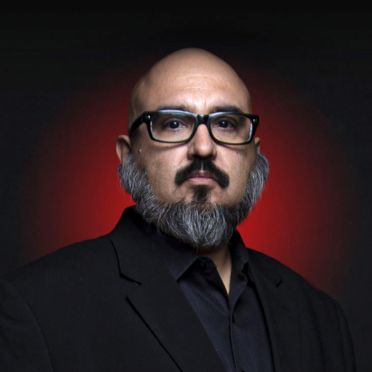 Headshot of Two Eagles Marcus, an Indigenous Native American man with glasses, a black mustache, and a salt-and-pepper beard, with a black suit.